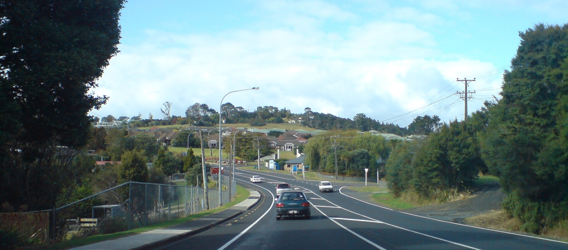 Whangaparaoa Peninsula Road on the Hibiscus Coast, with cars driving past suburban homes